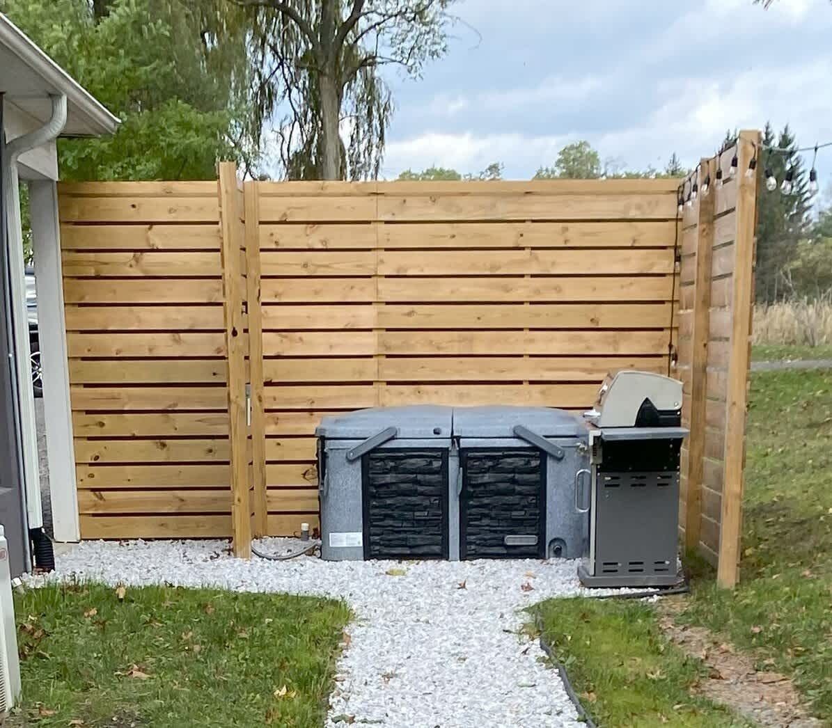 Une clôture en bois avec un barbecue et une poubelle devant.