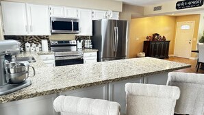 Una cocina con armarios blancos, electrodomésticos de acero inoxidable, encimera de granito y una zona de bar con sillas.