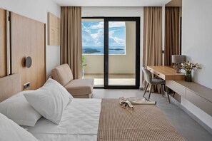 A hotel room with a bed, a desk, a chair, a view of the sea, and a balcony.
