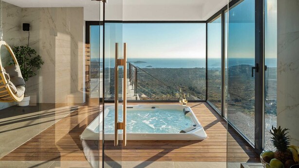 A modern spa area with a hot tub, wooden flooring, and a large glass window offering a scenic view of the landscape. - Luxury Villa Eloria with Pool (Rogoznica)