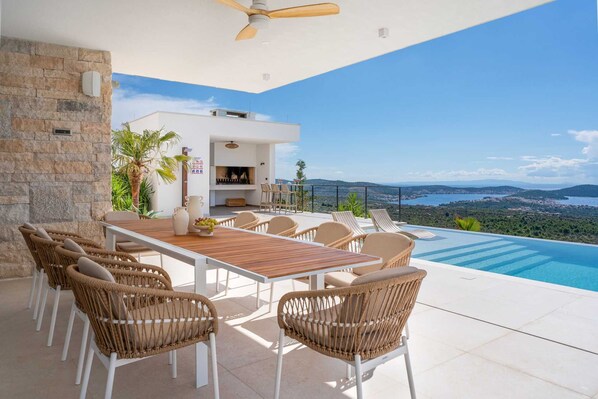 A modern outdoor dining area with a pool, stone wall, and a view of the landscape.