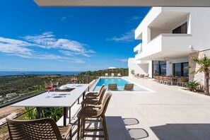 A modern outdoor dining area with a pool, overlooking a scenic landscape.