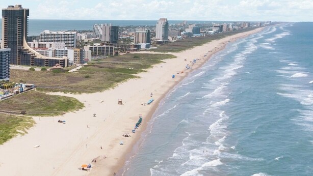 Un paysage urbain côtier avec une vaste plage, de hauts immeubles et un ciel dégagé.