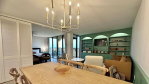 Un coin repas avec une table et des chaises en bois, un lustre et une vue sur le balcon.