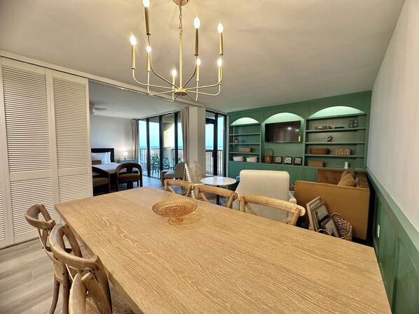 Un comedor con mesa y sillas de madera, una araña y vistas al balcón.
