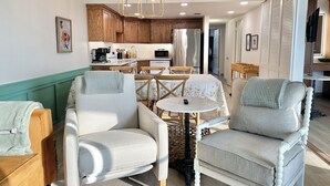 Un salon moderne avec deux fauteuils, une table ronde et une cuisine en arrière-plan.