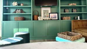 Une pièce aux murs de couleur turquoise, avec des étagères où sont exposés divers objets décoratifs, un tableau encadré et un téléviseur.