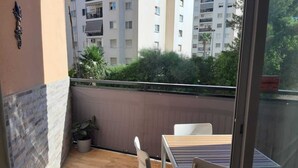 Un balcone con tavolo e sedie, una pianta in vaso e vista su un edificio a più piani.