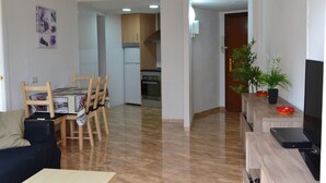 Un soggiorno moderno con zona pranzo, cucina sullo sfondo e televisore su un mobile in legno.