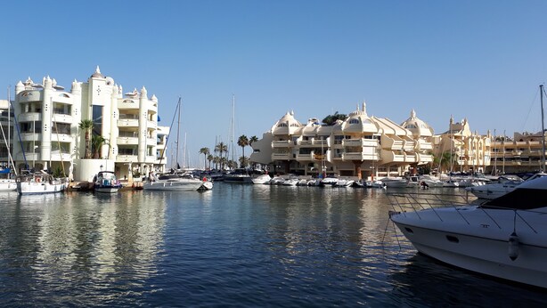 Una marina con yacht ormeggiati, circondata da edifici a più piani con balconi e palme.