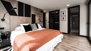 Un dormitorio moderno con una cama grande, dos lámparas de noche, una mesita de noche y vistas a la zona de la ducha.