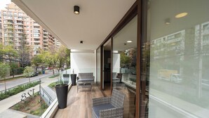 Un balcón con mobiliario de mimbre, una planta en maceta y vista a un paisaje urbano.