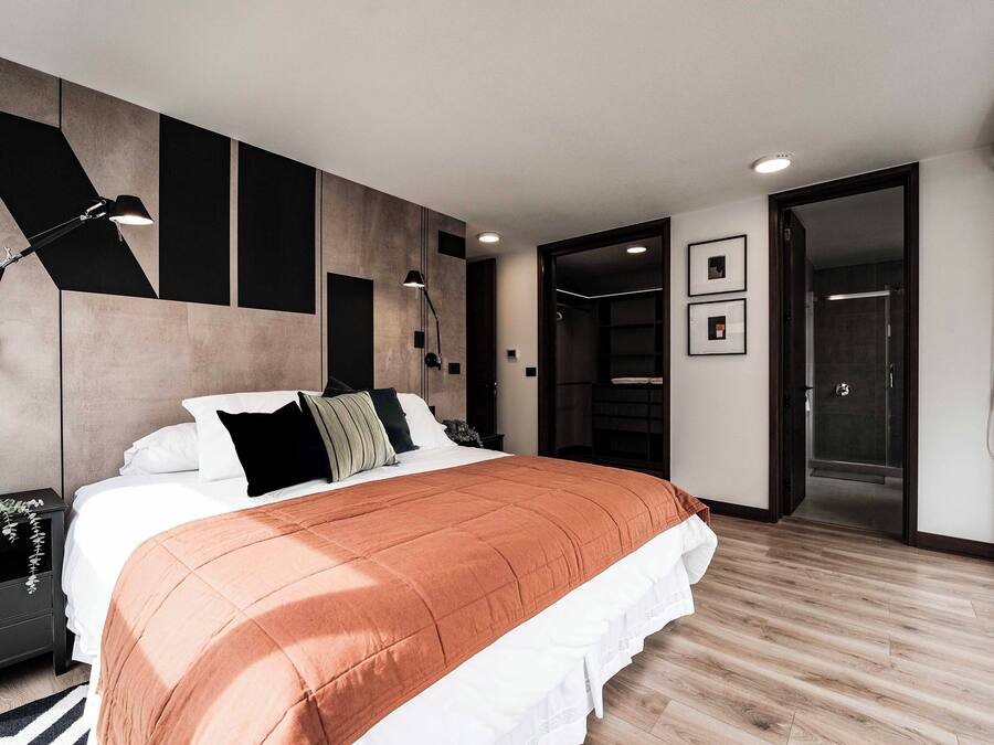 Ein modernes Schlafzimmer mit einem großen Bett, Nachttischen, einer Wandlampe und einem begehbaren Kleiderschrank.