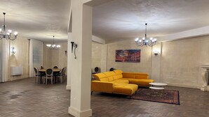 A spacious living area with a herringbone wood floor, a yellow sectional sofa, a dining table with chairs, and a fireplace. - Villa Brikinnia (Lentini)