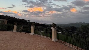 A terrace with a brick floor and a metal railing, overlooking a hilly landscape with a sunset sky. - Villa Brikinnia (Lentini)