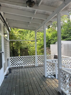 A covered porch with white lattice railings, a wooden deck, and a view of a green, leafy garden. - Relax and escape in this vibrant Columbus apartment (Columbus)
