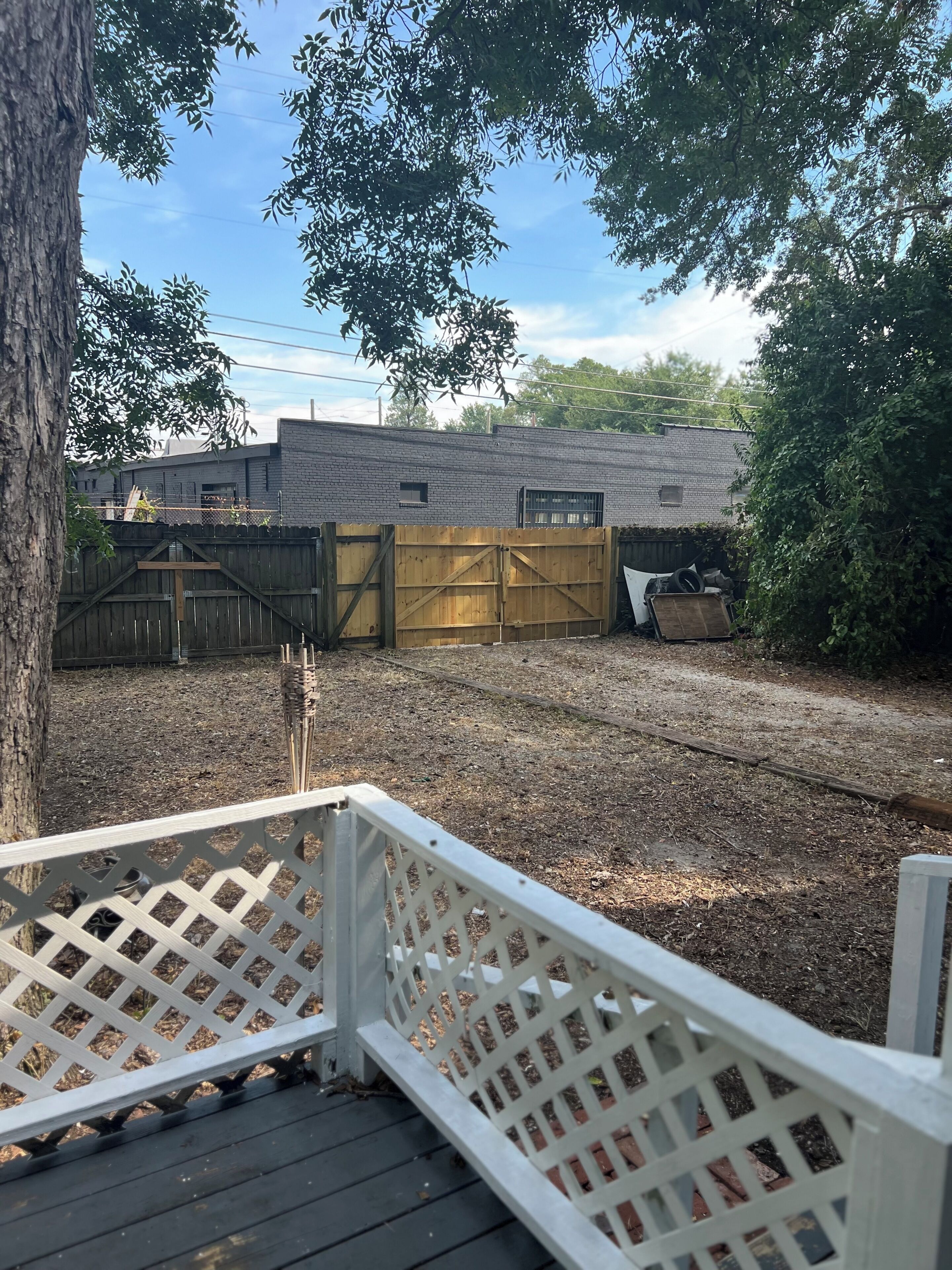 A backyard with a wooden deck, a brick building, and a metal gate.