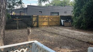 A backyard with a wooden deck, a brick building, and a metal gate.