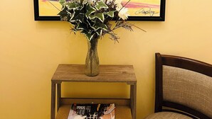 A framed painting of a tropical beach scene with palm trees and a sunset, placed above a wooden side table with a magazine and a vase of plants. - Relax and escape in this vibrant Columbus apartment (Columbus)
