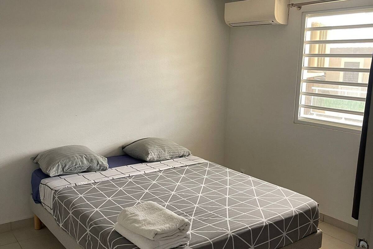 A neatly made bed with a geometric patterned bedspread, a folded towel, and two pillows.