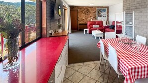 Un espace repas avec des nappes à carreaux rouges et blancs, des chaises en cuir rouge et une vue sur l’extérieur.