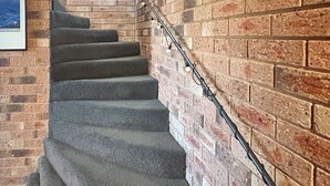 Un escalier dont les marches sont recouvertes de moquette, menant à un mur en briques.
