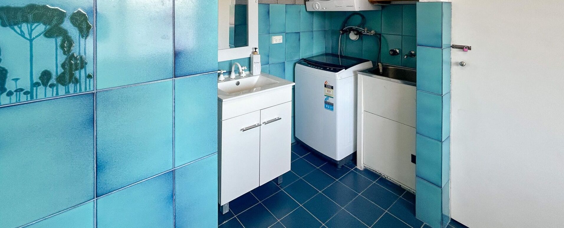 Une cuisine de taille réduite, avec des carreaux bleus, un évier, un petit réfrigérateur et une cuisinière.