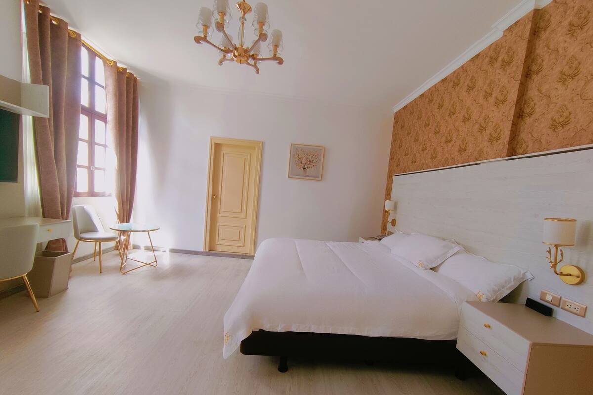 A hotel room with a bed, bedside table, lamp, chair, and a desk.