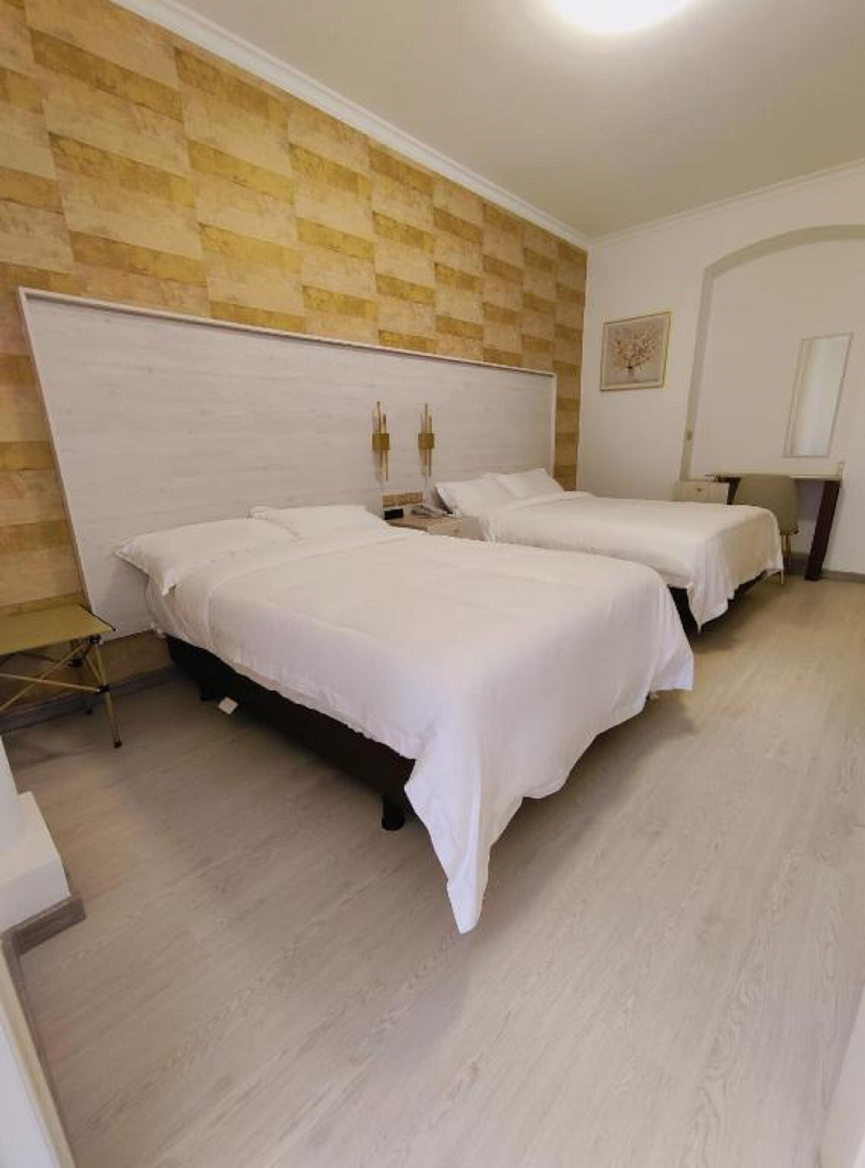 Habitación de hotel con dos camas, cabecero de madera, una mesita y una silla.