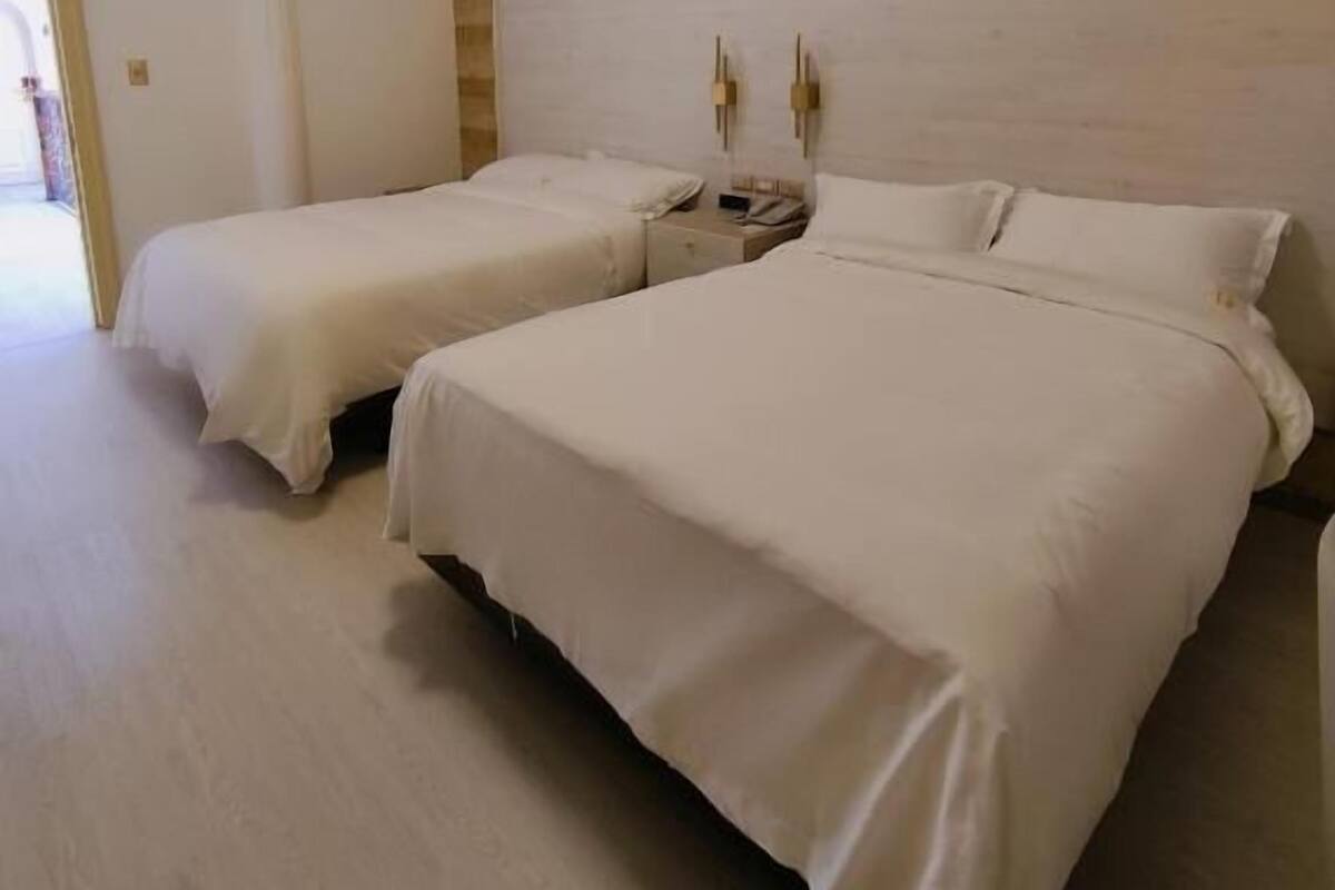 A hotel room with two beds, a wooden headboard, a ceiling light, and a door leading to another room.