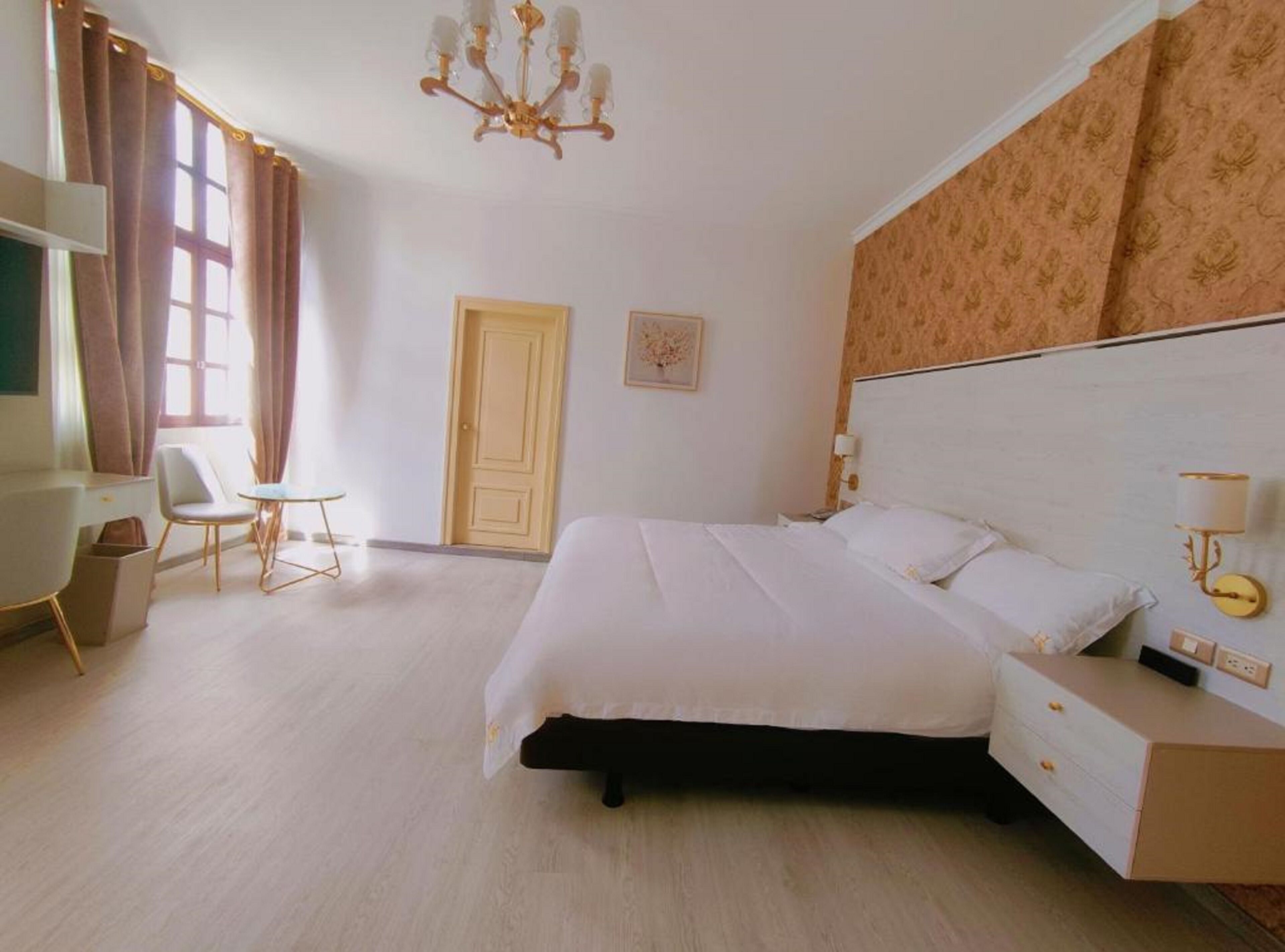 Habitación de hotel con cama, mesita de noche, lámpara, silla y una puerta.
