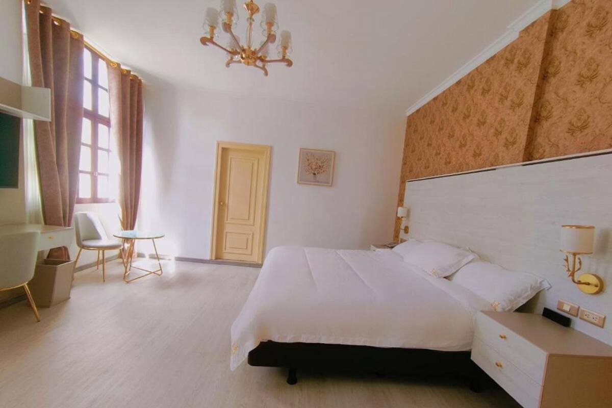 A hotel room with a bed, bedside table, lamp, chair, and a door.