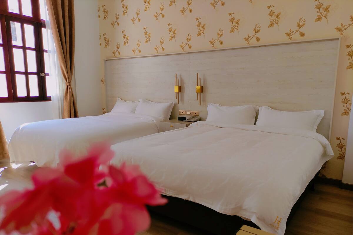 A hotel room with two beds, a wooden floor, and a floral wallpaper pattern.