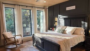 Un dormitorio con una cama grande, un sillón mecedora y vistas al exterior a través de amplios ventanales.