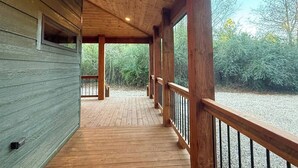 Una terraza de madera con barandilla, rodeada de follaje.