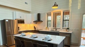 Una cocina moderna con una isla grande, electrodomésticos de acero inoxidable y una ventana con persianas.
