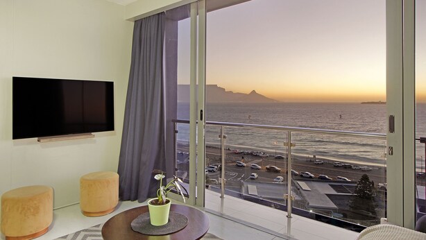 Et moderne hotelværelse med en stor balkon, et fladskærms-TV og udsigt til havet samt parkeringsområdet.