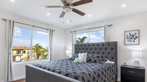 A bedroom with a large bed, a ceiling fan, and a nightstand with a lamp. - Oxnard Beach Retreat  (Oxnard)