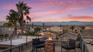 A rooftop patio with a fire pit, outdoor seating, and a view of a residential area with mountains in the background. - Oxnard Beach Retreat  (Oxnard)