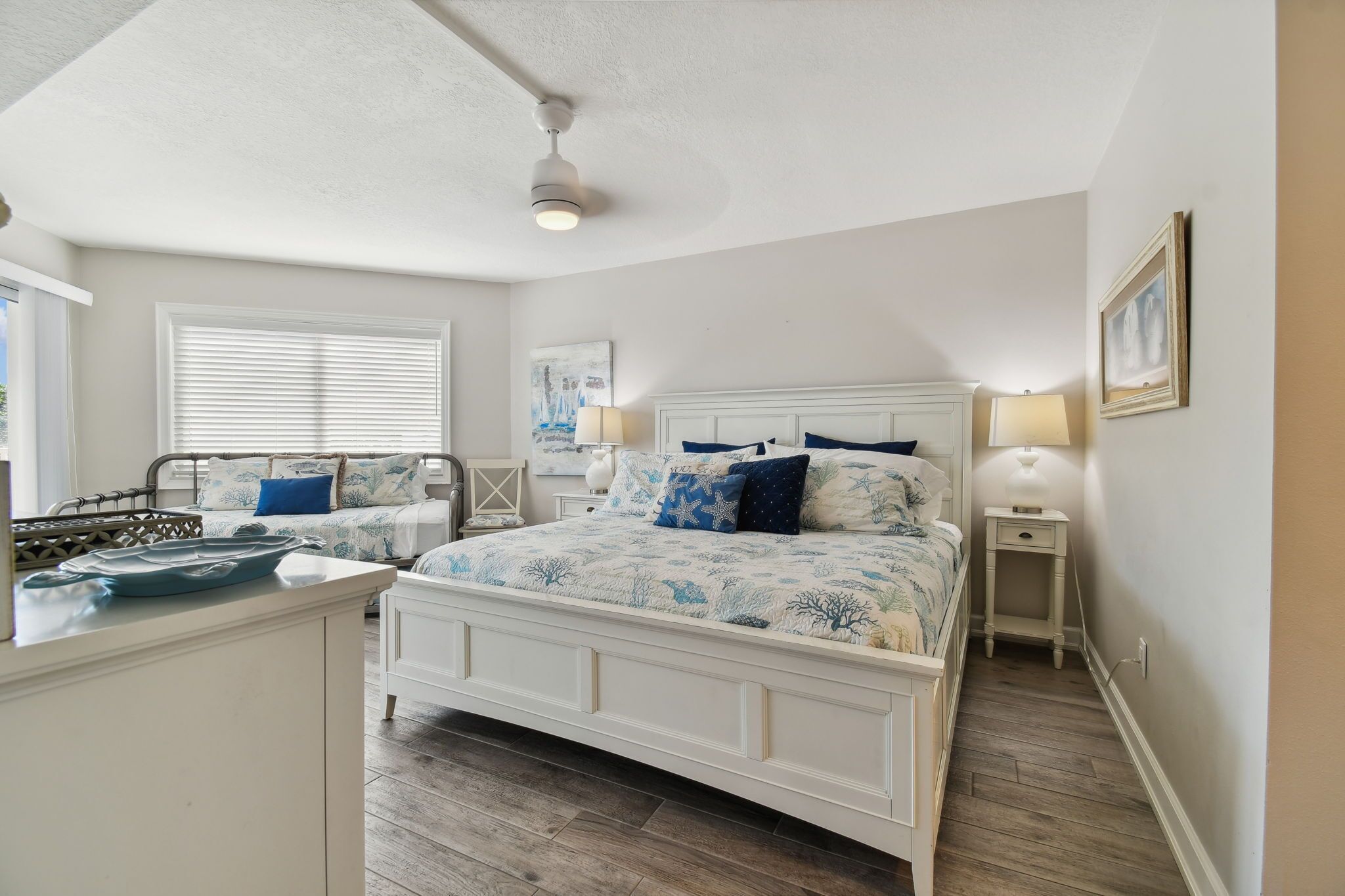 A bedroom with a large bed, two bedside tables, a ceiling fan, and a window with blinds.