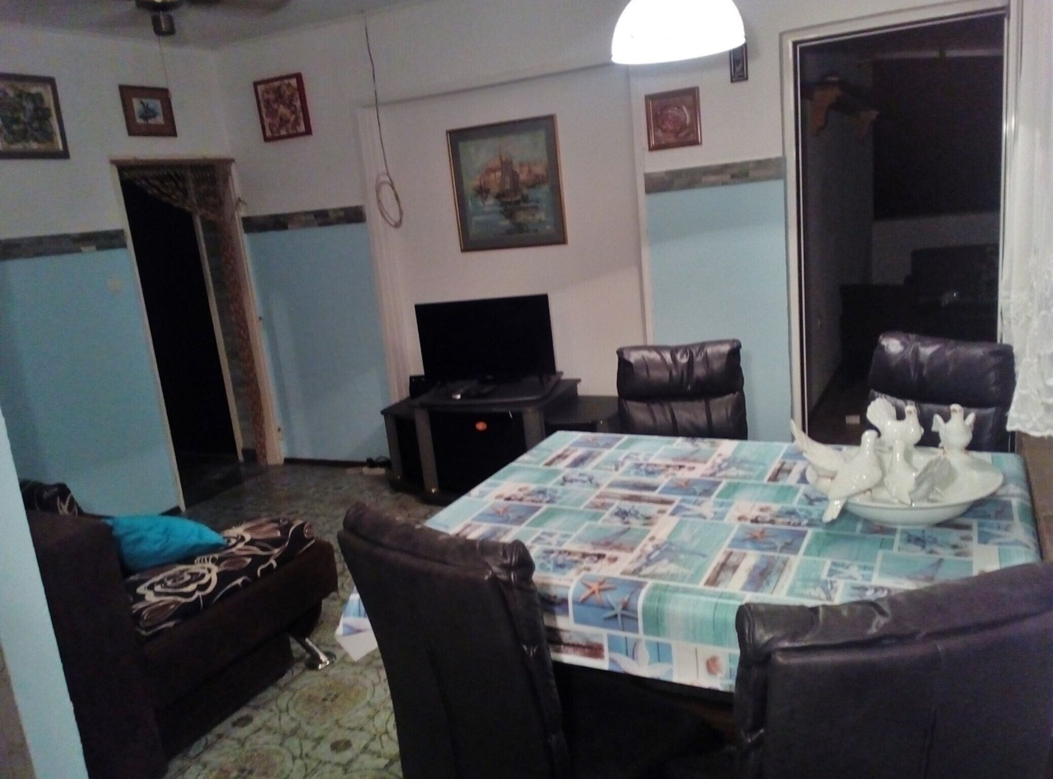 Un salon comprenant une table à manger, des fauteuils en cuir, un canapé, un téléviseur et un tableau accroché au mur.