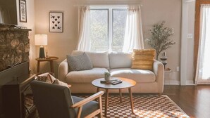 A cozy living room with a sofa, armchair, and coffee table, a fireplace, and a ceiling fan.