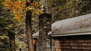 A stone pathway leading to a wooden building with a stone chimney, surrounded by autumn foliage.