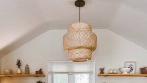 A kitchen with white cabinets, a black countertop, a window with blinds, and a hanging light fixture.