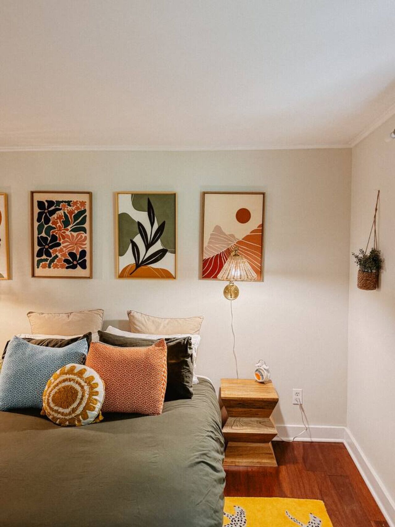 A bedroom with a bed, pillows, a nightstand, a lamp, and wall art.