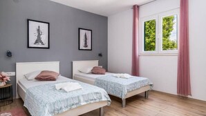 Une chambre avec deux lits simples, des murs gris et une fenêtre avec des rideaux roses.