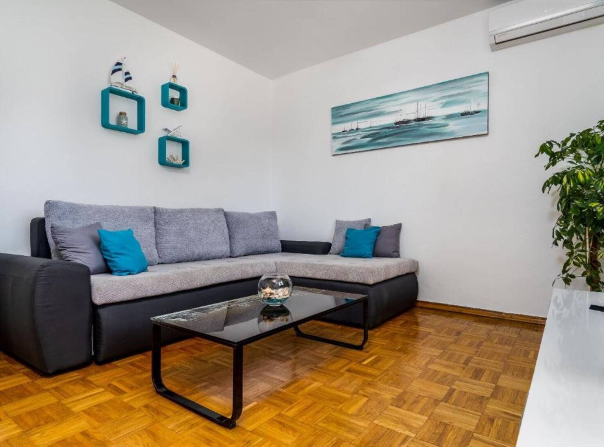 A modern living room with a grey sofa, a glass coffee table, and a painting of a sailboat on the wall.