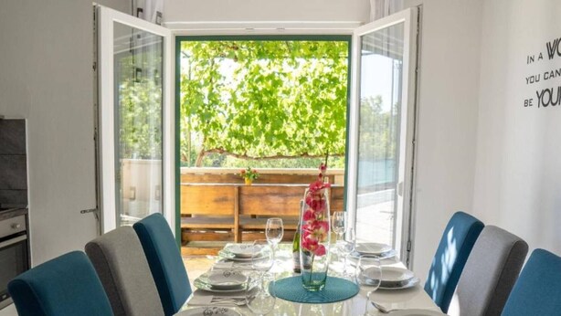 Un espace repas avec une table dressée pour quatre personnes, une cloison en verre et une vue sur la verdure à l’extérieur.