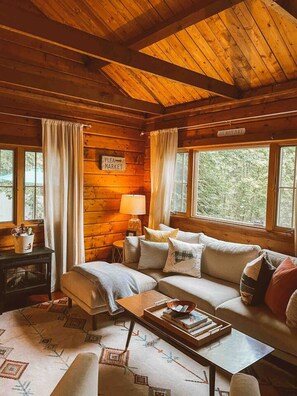 A cozy cabin interior with a wooden ceiling, a sofa, a coffee table, and a sign reading "Our Happy Place". - The Little Lake Cabin with hot tub (New Fairfield)