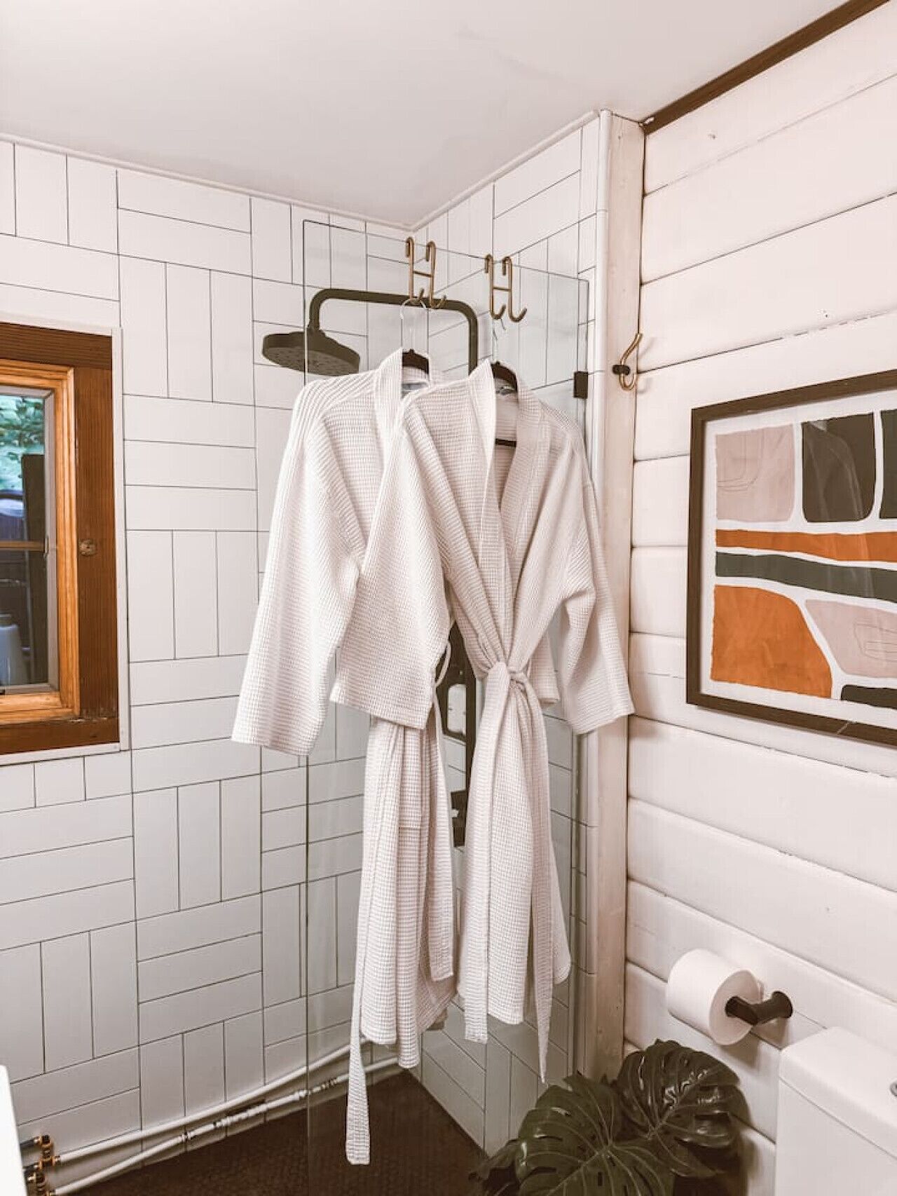 Une salle de bain avec des murs recouverts de carreaux blancs, une porte en bois et un tableau abstrait encadré.